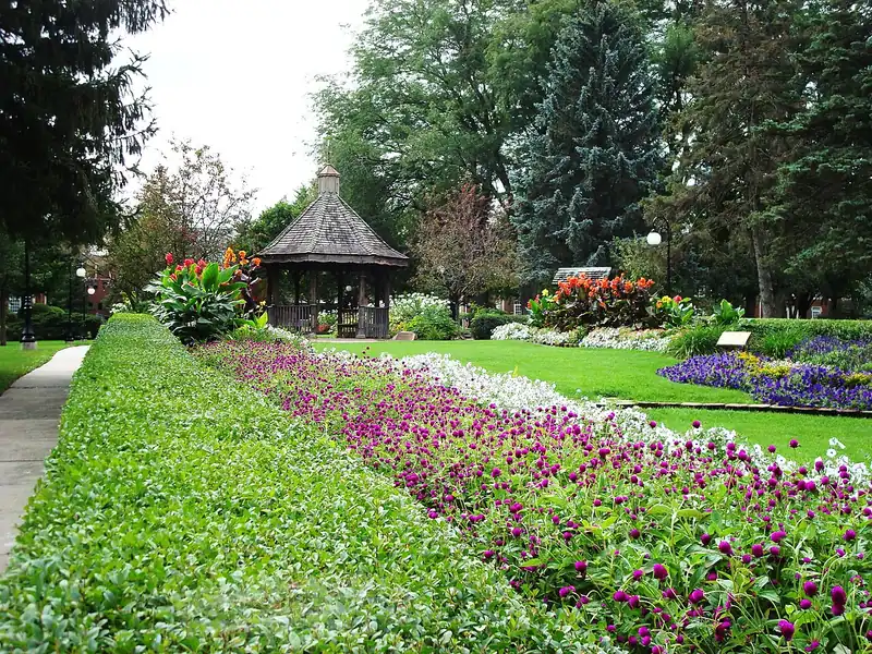 Gazebo in Buxton Park with beds of pink and purple flowers and tall trees