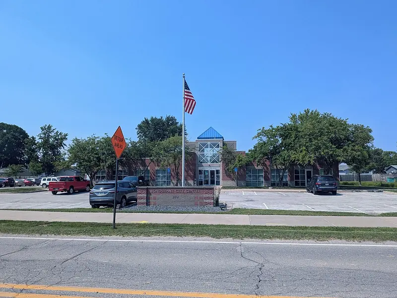 Bondurant City Center building with a flagpole, landscaping and a parking lot under a blue sky