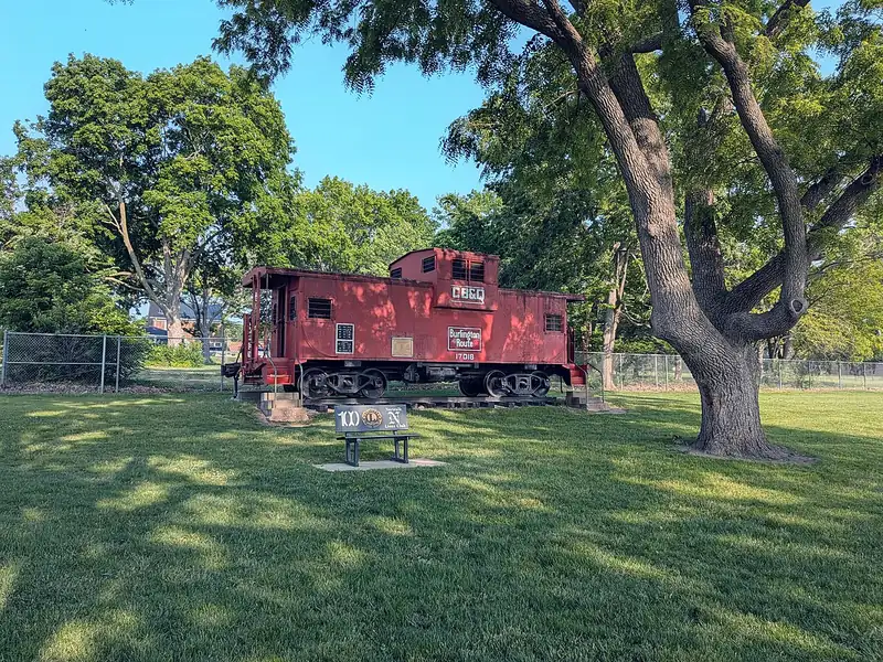 Red Burlington Route caboose on display under large shade trees in a city park