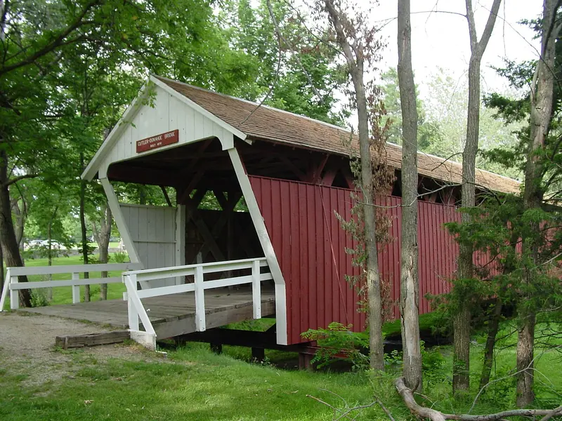 Red Cutler-Donahoe covered bridge with white trim among trees in Winterset City Park
