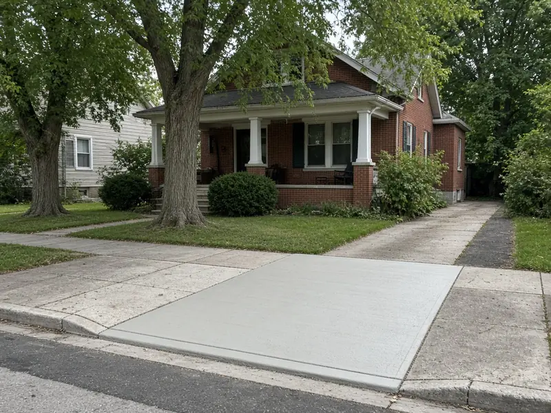 New concrete driveway approach and curb cut crossing the public sidewalk in front of a red brick bungalow