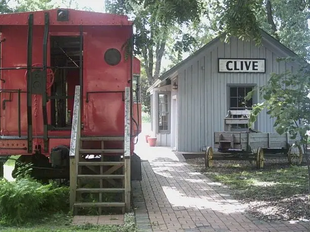 Restored gray wooden train depot with a CLIVE sign beside a red caboose